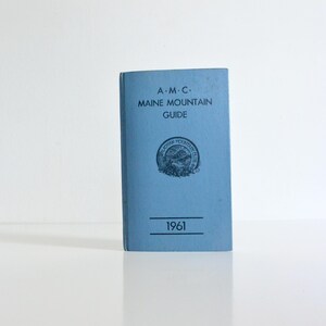 May include: A blue book titled "A.M.C. Maine Mountain Guide" with a seal and the year 1961 printed on the cover.