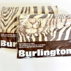 May include: Two packages of twin-sized bedding with a zebra print and a tiger face design. The packaging is brown with white text that reads "One twin fitted sheet for 39x75 in. mattress" and "One twin flat sheet or 30x75 in. to 39x75 in mattress 66x104 in. size before hemming". The bottom of the package reads "Burlington #".