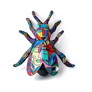 Puede incluir: Un insecto abstracto colorido con un cuerpo negro y alas multicolores. Las alas están decoradas con patrones geométricos y caras estilizadas.