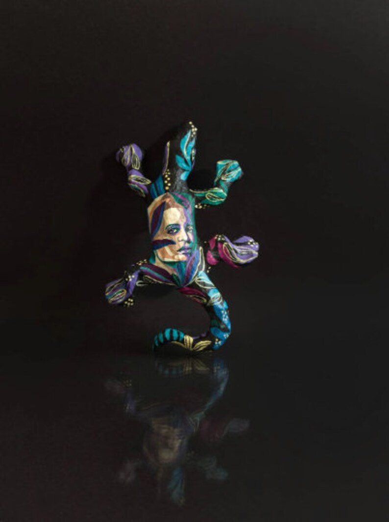 May include: A colorful, hand-painted ceramic lizard figurine with a human face and floral patterns in shades of blue, green, purple, and gold.