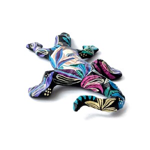 May include: A black painted gecko figurine with a colorful floral design. The gecko is lying on its belly with its tail curled up.