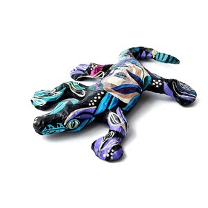 May include: A hand-painted paper mache lizard figurine with a black base and colorful floral patterns in shades of blue, purple, and gold.