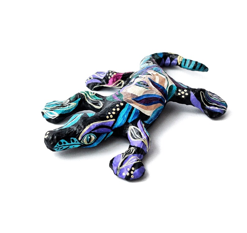 May include: A hand-painted paper mache lizard figurine with a black base and colorful floral patterns in shades of blue, purple, and gold.