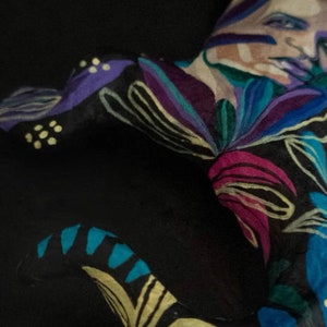 May include: A person with their body painted in a colorful floral pattern. The pattern includes shades of blue, purple, pink, yellow, and green. The person's face is also painted with a floral design.