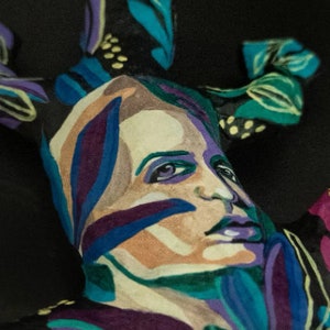 May include: A colorful abstract painting of a face with blue, green, purple, and white paint. The face is surrounded by abstract shapes and patterns.