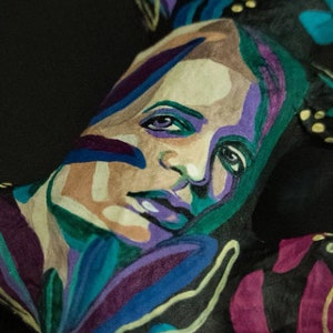 May include: A close-up of a person's face painted with colorful abstract designs. The face is painted with shades of blue, green, purple, and yellow. The person's eyes are closed and their lips are painted a light purple.