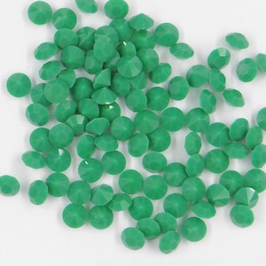 Puede incluir: Una dispersión de pequeños diamantes de imitación redondos de color verde. Los diamantes de imitación tienen una apariencia facetada, similar a la de un diamante.