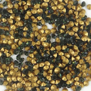 Peut inclure: Gros plan sur une grande quantité de strass dorés et vert foncé. Les strass sont éparpillés sur une surface blanche.