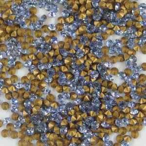Peut inclure: Gros plan sur une collection de petits ornements scintillants. L'image présente un mélange de strass bleu clair et dorés, dispersés sur la surface. Les strass sont ronds et facettés, captant la lumière.