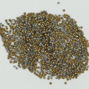 Könnte beinhalten: Ein Haufen kleiner, goldener und silberner Strasssteine. Die Strasssteine sind auf einer weißen Oberfläche verstreut.