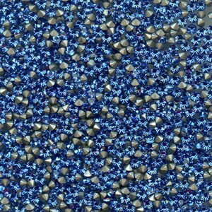 Op de afbeelding: Een close-up van een grote hoeveelheid blauwe strass steentjes met zilveren settings. De strass steentjes zijn in een willekeurig patroon gerangschikt.