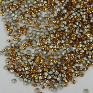 Peut inclure: Une image en gros plan d'un tas de petits strass ronds et facetés. Les strass sont un mélange de couleurs argent et or.