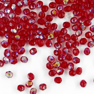 Peut inclure: Une dispersion de perles de verre rouge irisées. Les perles sont facettées et ont une surface brillante et réfléchissante.