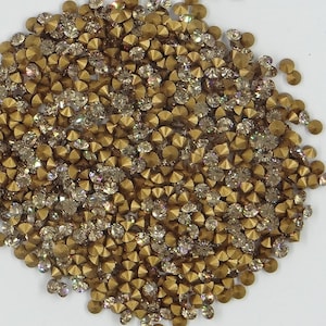 Peut inclure: Un grand tas de strass de couleur or avec une finition claire et irisée. Les strass ont un dos pointu, ce qui les rend adaptés à l'artisanat et à l'embellissement de projets.