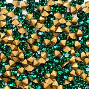 Peut inclure: Une collection de nombreux petits cristaux ronds à facettes vert émeraude avec des dos pointus de couleur or métallique. Les cristaux sont disposés en un motif dense et dispersé, mettant en valeur leurs surfaces réfléchissantes.