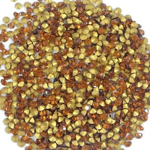 Peut inclure: Gros plan sur une collection de petits strass facettés. Les strass sont un mélange de jaune doré et de brun ambré, créant un effet scintillant. Les pierres précieuses sont dispersées sur la surface.