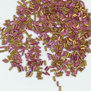 Peut inclure: Une grande quantité de strass rectangulaires en verre rose et or. Les strass sont éparpillés sur une surface blanche.
