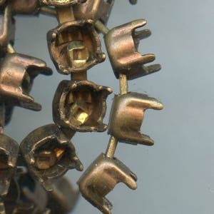 Peut inclure: Gros plan sur une section d'un composant de bijou en laiton vintage. Le composant présente de multiples sertissages à dos ouvert, chacun conçu pour contenir une pierre précieuse. Les sertissages sont reliés par de fines tiges en laiton.