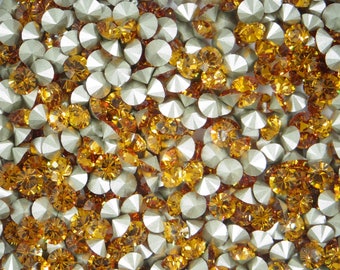 Puede incluir: Una imagen de primer plano de una gran cantidad de pequeños diamantes de imitación redondos y facetados. Los diamantes de imitación son una mezcla de colores plateado y ámbar.