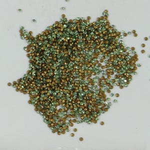 Könnte beinhalten: Ein großer Haufen grüner und goldener Strasssteine. Die Strasssteine sind klein und haben eine spitze Form.