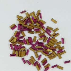 May include: A large pile of small, rectangular, gold-coloured rhinestones with a pink iridescent finish.