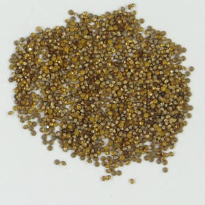 Peut inclure: Un grand tas de petits strass dorés. Les strass sont éparpillés sur une surface blanche.