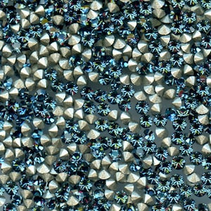 Op de afbeelding: Een close-up van een oppervlak bedekt met zilveren en blauwe strass steentjes. De strass steentjes zijn in een willekeurig patroon gerangschikt en zijn allemaal even groot.