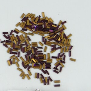 May include: A large pile of small, rectangular, iridescent rhinestones. The rhinestones are a mix of gold and purple.