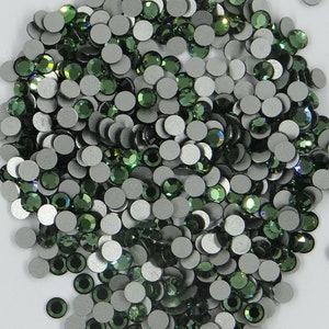 Può includere: Un grande mucchio di strass verde scuro con retro argentato. Gli strass sono sparsi su una superficie bianca.