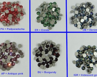 May include: Six piles of colorful rhinestones with adhesive backs. The colors are padparadscha, erinite, denim blue, burgundy, antique pink, and iridescent green.