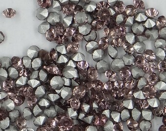 May include: A close-up of a large quantity of small, faceted rhinestones. The rhinestones are a mix of silver and light pink.