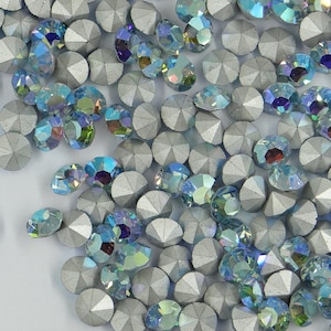 Op de afbeelding: Een close-up van een grote hoeveelheid zilveren en blauwe strass steentjes. De strass steentjes zijn verspreid over een wit oppervlak.