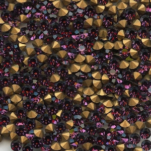 Peut inclure: Gros plan sur une collection de strass violets et dorés. Les strass ont un aspect facetté, semblable à des bijoux, avec une couleur violet foncé et une base dorée métallique. L'arrangement est dense, créant une surface texturée.