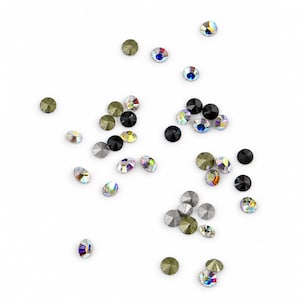 Peut inclure: Une collection de petits strass ronds à facettes dispersés sur une surface blanche. Les pierres présentent diverses finitions, notamment noir uni, or métallique, argent mat et des cristaux transparents irisés aux reflets arc-en-ciel.