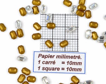 Puede incluir: Una colección de cuentas rectangulares facetadas en acabados oro metálico y cristal transparente, esparcidas alrededor de un papel milimetrado con una etiqueta que indica que 1 cuadrado equivale a 10mm, ofreciendo una escala clara para estos componentes.