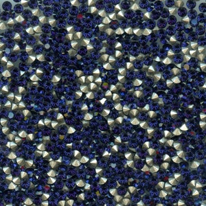 Peut inclure: Gros plan sur une collection de petits strass ronds et facettés. Les strass sont principalement d'un bleu foncé profond avec des facettes argentées. L'arrangement est dense, créant une surface texturée et scintillante. Idéal pour les projets d'artisanat.