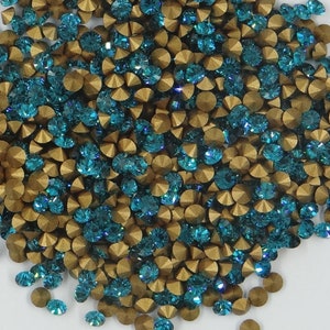 Peut inclure: Un grand tas de strass bleu sarcelle et or. Les strass sont petits et ont un design facetté.