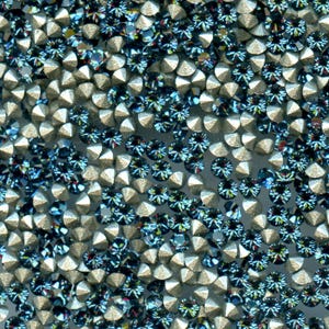 Peut inclure: Gros plan sur une collection de petits strass étincelants. Les strass sont un mélange d'argent et de bleu foncé, avec une coupe à facettes qui capte la lumière. L'arrangement est dense, créant une surface texturée.