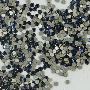 May include: A collection of small, circular rhinestones. The rhinestones are a mix of silver and dark blue, with a reflective, shiny surface. The image is a close-up, showing the details of the individual stones.