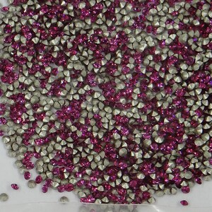 Op de afbeelding: Een close-up van een grote hoeveelheid kleine, ronde, gefacetteerde strass steentjes. De strass steentjes zijn een mix van zilver en roze.