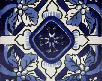 May include: Blue and white ceramic tile with a floral pattern. The tile features a central diamond shape with a stylized flower design. The corners of the tile are decorated with stylized leaves and flowers.