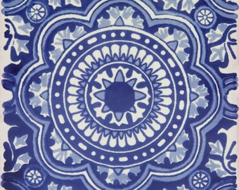 May include: Square ceramic tile with a symmetrical blue and white floral design. The pattern features a central starburst, surrounded by concentric circles and stylized floral motifs. The tile has a vintage, handcrafted aesthetic.