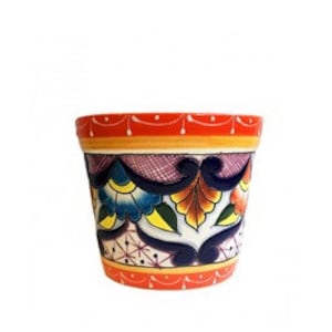 Op de afbeelding: Een keramische bloempot met een handgeschilderd ontwerp met een feloranje rand, ingewikkelde donkerblauwe krulpatronen en veelkleurige bloemmotieven in geel, groen en rood op een witte achtergrond met gearceerde details.