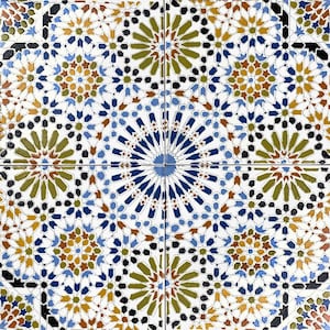 Op de afbeelding: Een witte tegel met een geometrisch patroon in tinten blauw, groen, bruin en goud. Het patroon bestaat uit herhalende vormen en sterren.
