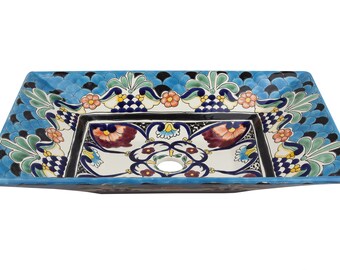 May include: A square ceramic sink with a blue, green, and white floral design. The sink has a drain hole in the center.