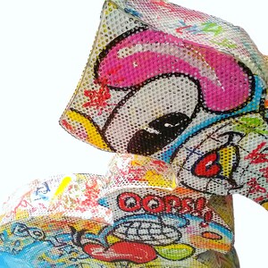 May include: A colorful, three-dimensional sculpture made of mesh and painted with a variety of bright colors and patterns. The sculpture features a cartoon-like face with a pink nose and a red mouth. The sculpture is titled "Oops!" in a black and white speech bubble.