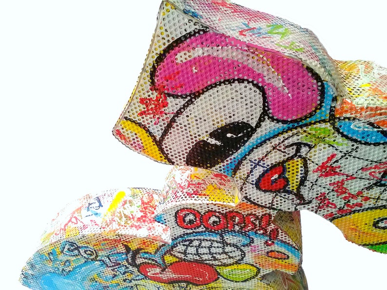 May include: A colorful, three-dimensional sculpture made of mesh and painted with a variety of bright colors and patterns. The sculpture features a cartoon-like face with a pink nose and a red mouth. The sculpture is titled "Oops!" in a black and white speech bubble.