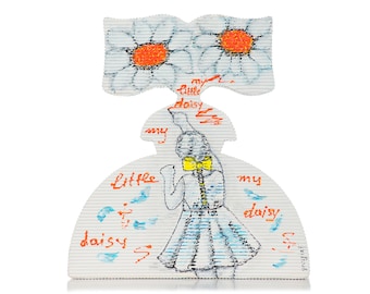 May include: A white paper cutout of a girl in a blue dress holding a white daisy with an orange center. The girl is wearing a yellow bow and the text "my little daisy" is written on the paper.