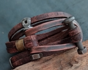 May include: A brown leather bracelet with metal accents. The bracelet has a unique design with multiple layers of leather and metal hardware.