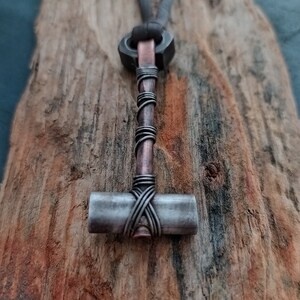 May include: A silver and copper hammer pendant necklace with a leather cord. The hammer is wrapped with copper wire.